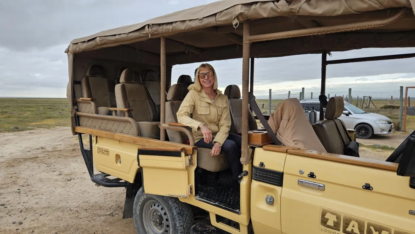 Maria Faires, RD, sitting in an open-sided safari vehicle in the Kenyan savanna, showcasing field-tested travel expertise.
